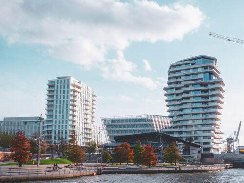 Haus der HafenCity, davor Wasser. Im Hintegrund Kräne.