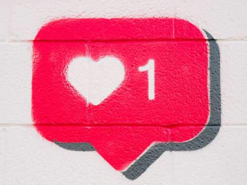 Graffiti eines Like-Sympols von Instagram; Darunter eine Hand mit Smartphone