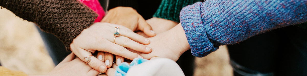 Frauen mit verschiedenen farbigen Pullovern legen ihre Hände in der Mitte zusammen um "Zusammenarbeit und Teamgefühl" zu symbolisieren
