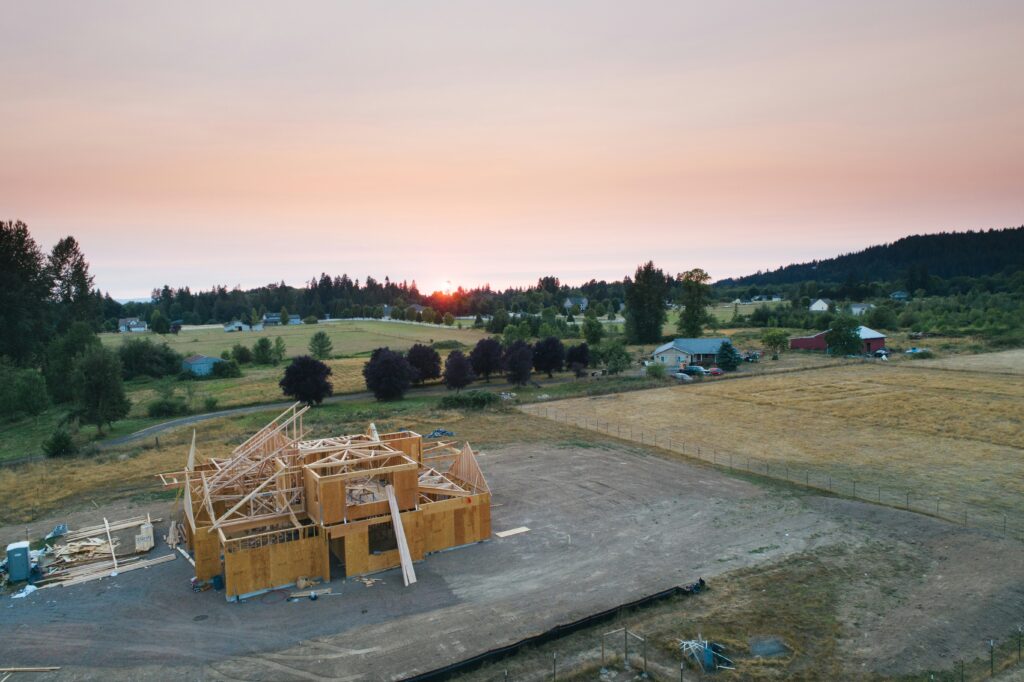 Zu sehen ist eine Landschaft, bestehend aus einzelnen Grundstücken. Im Vordergrund ein Holzhaus im Bau. Im Hintergrund mehrere Freiflächen und Grünstrukturen.