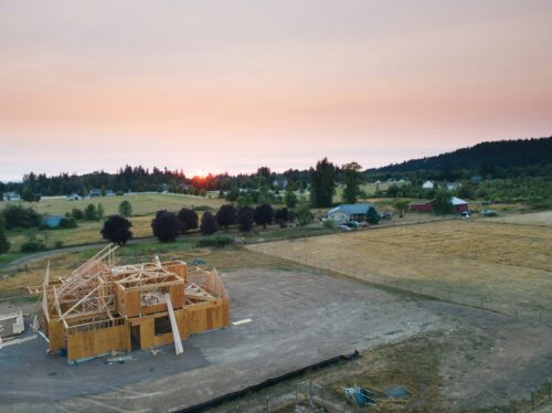 Zu sehen ist eine Landschaft, bestehend aus einzelnen Grundstücken. Im Vordergrund ein Holzhaus im Bau. Im Hintergrund mehrere Freiflächen und Grünstrukturen.